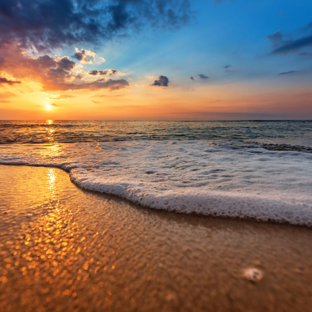 A sunset over the ocean with waves crashing on it.